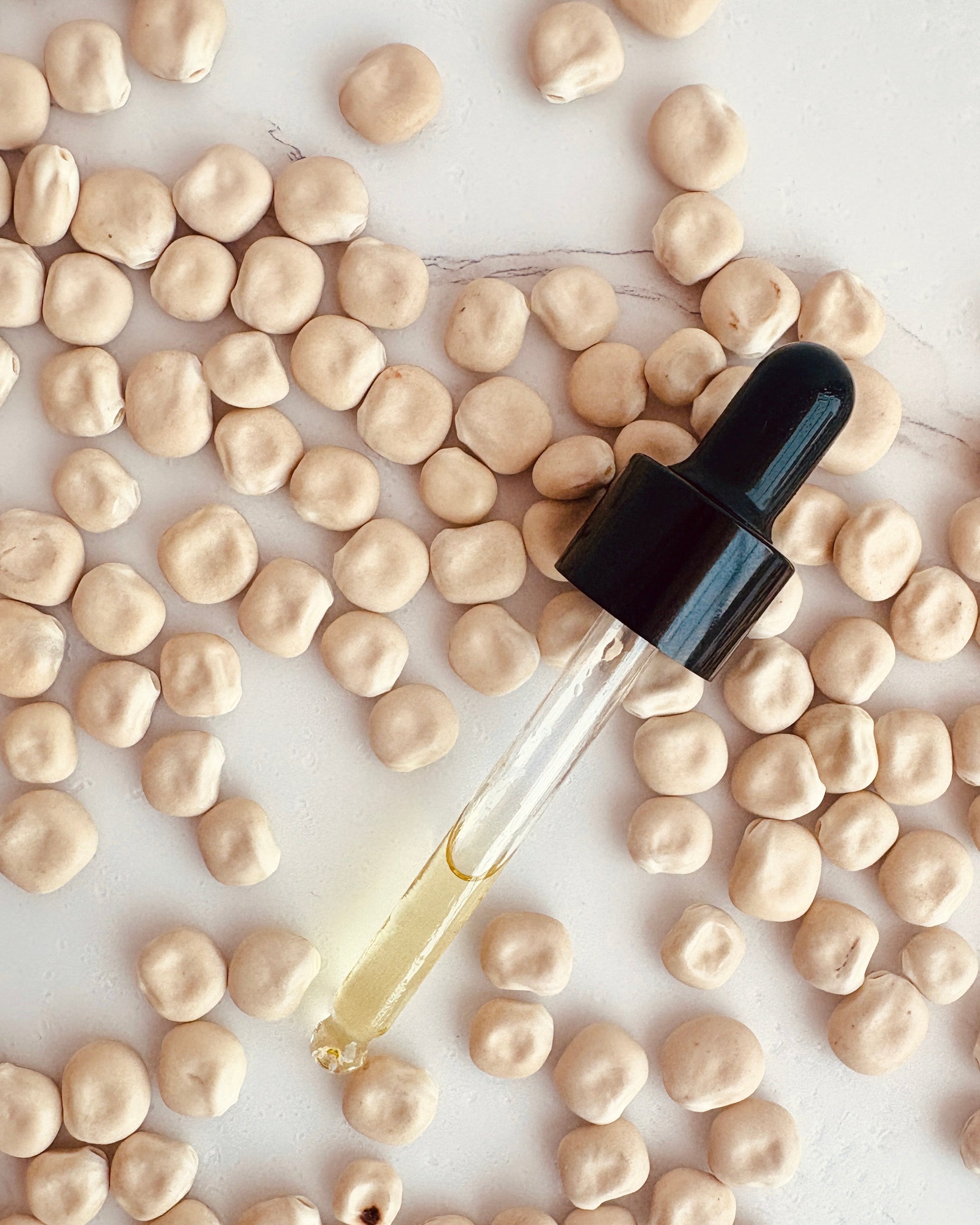 A clear glass dropper bottle filled with pale yellow liquid, placed diagonally on a white surface and surrounded by scattered Lupin seeds.