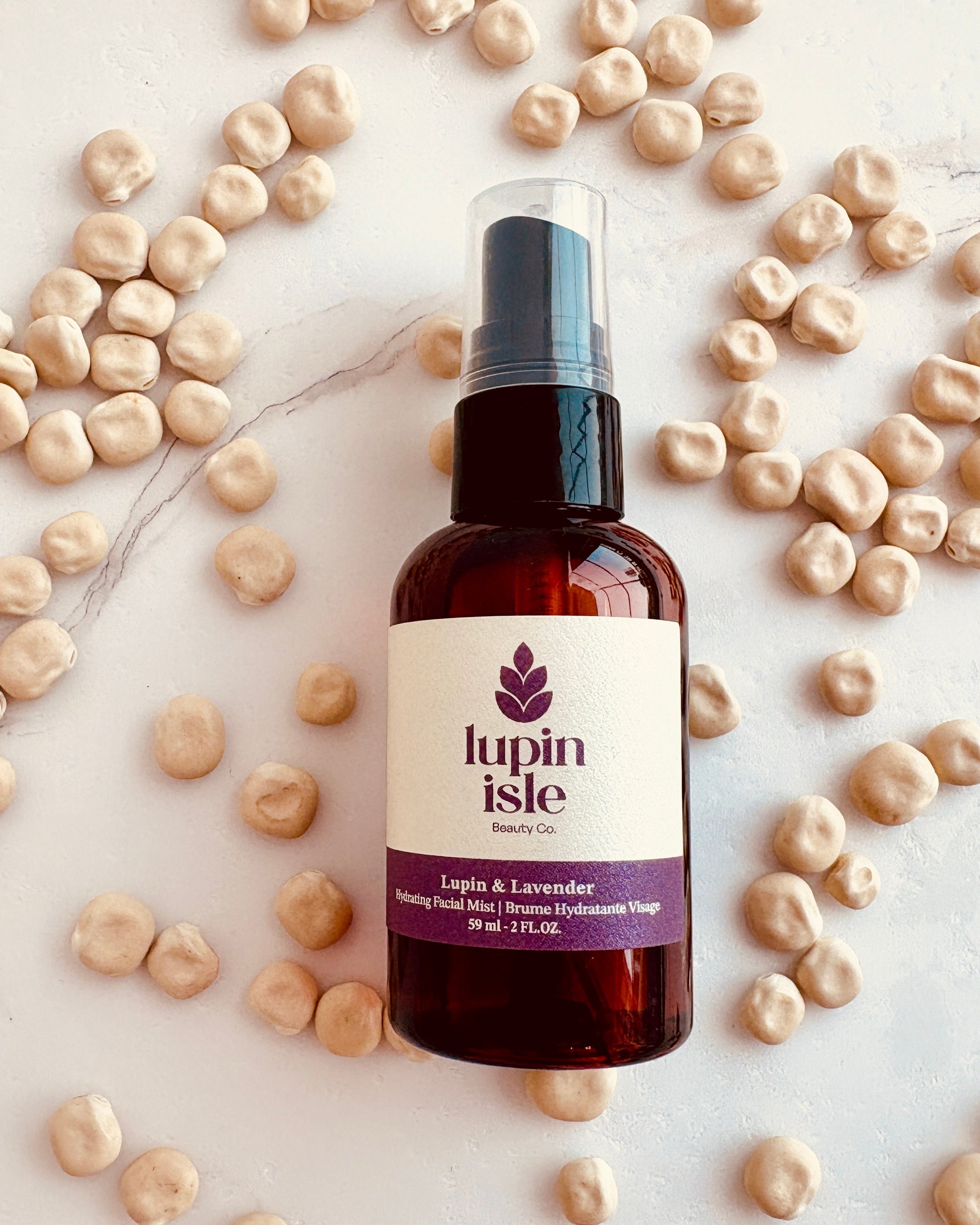 A bottle of Lupin Isle facial Mist with a white label and purple text, placed on a light marble surface and surrounded by scattered beige lupin beans.