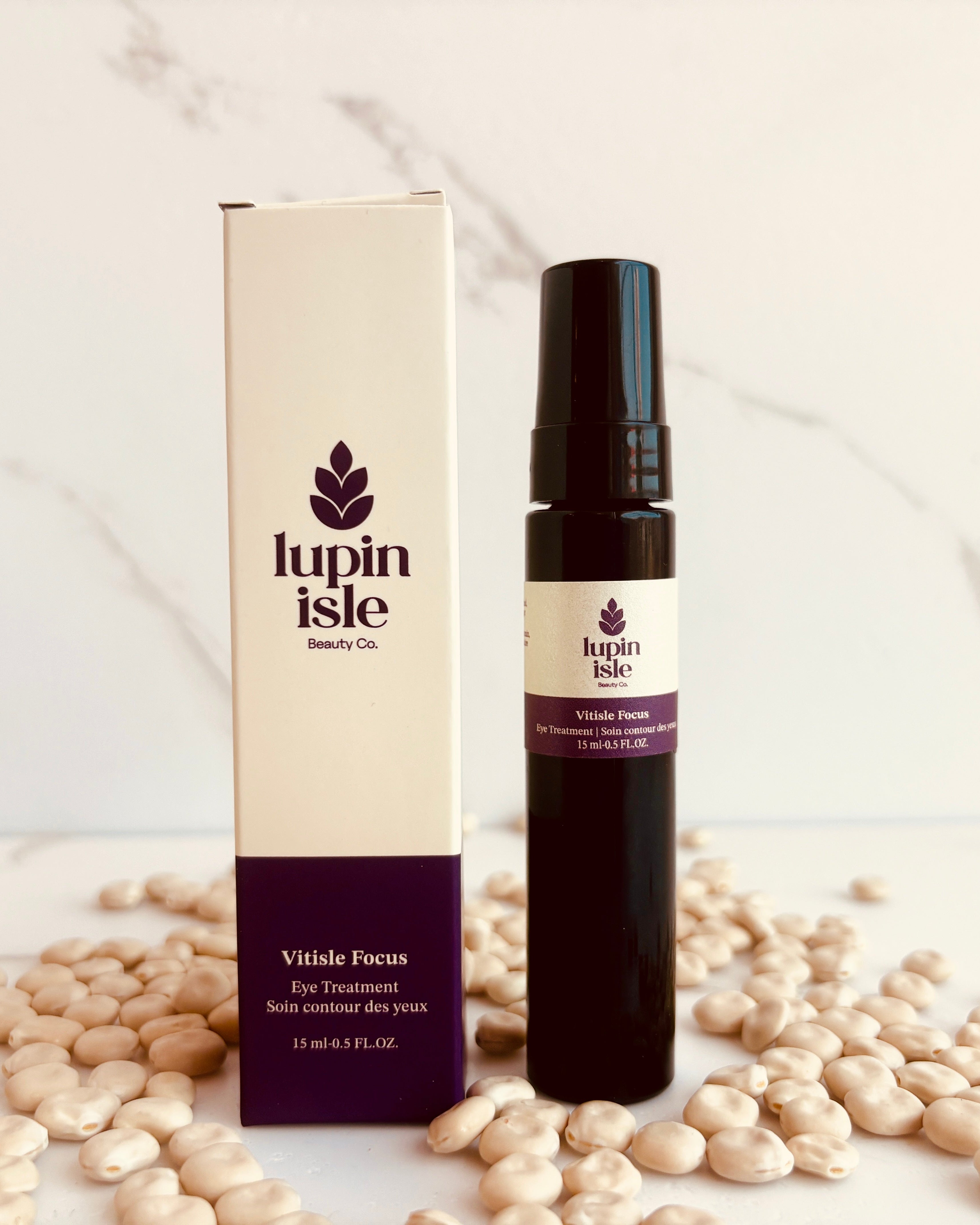 A bottle of Lupin Isle Vitise Focus Eyewear Solution next to its white and purple packaging box, styled on a white marble surface surrounded by scattered lupin beans.