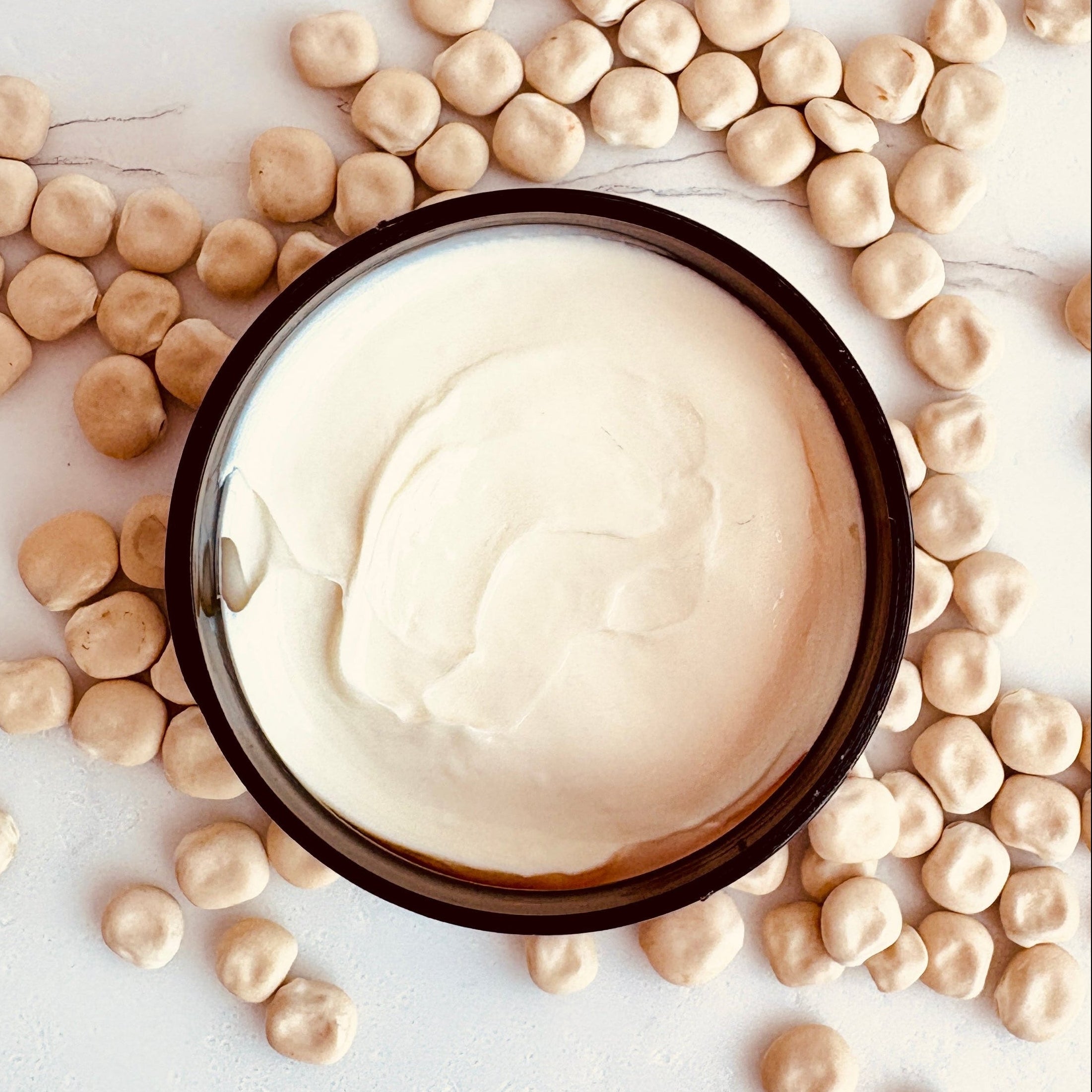 A jar of opened Lupin Isle Velvet Body Butter displaying the creamy texture, surrounded by scattered lupin seeds on a light neutral background.
