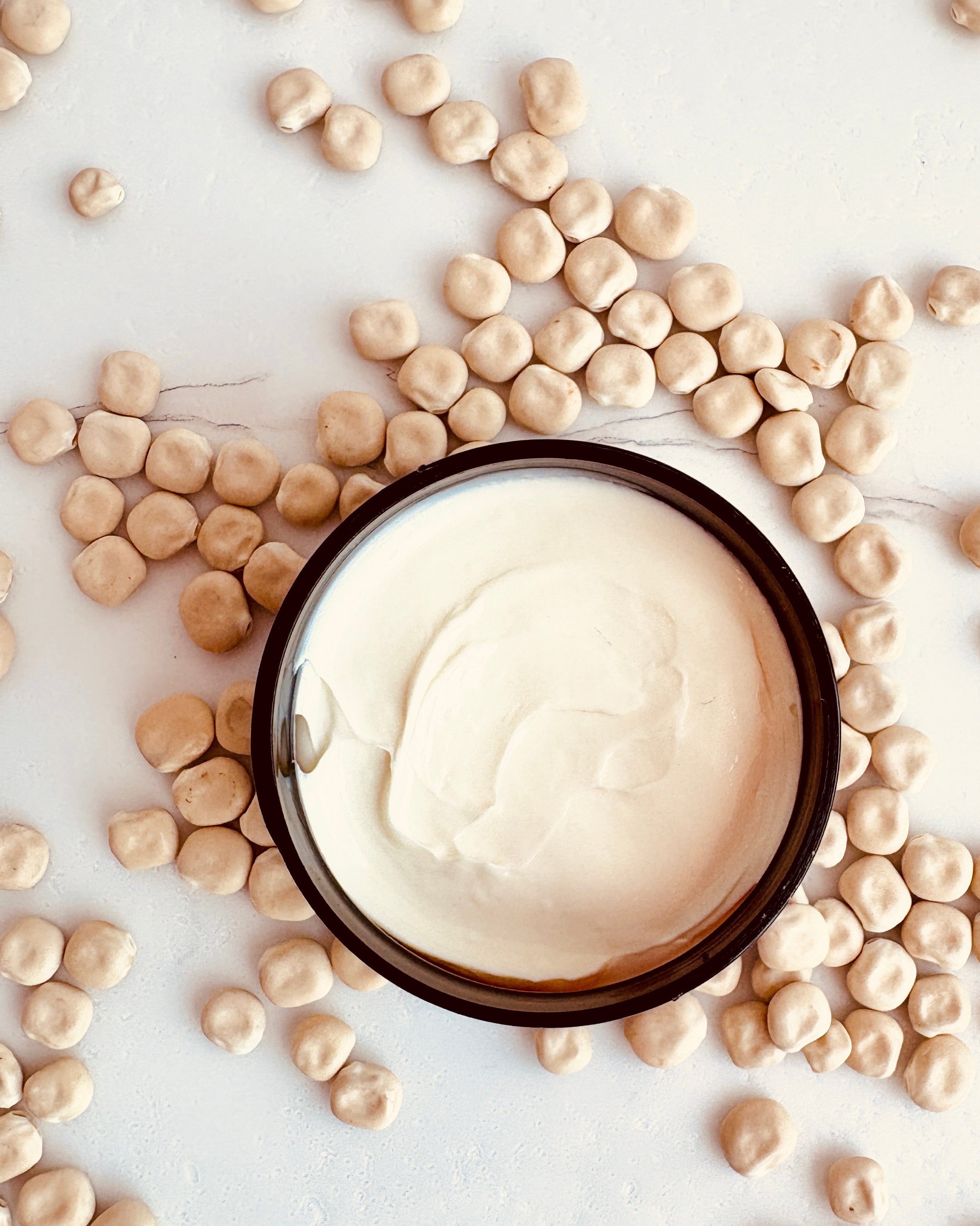 A jar of opened Lupin Isle Velvet Body Butter displaying the creamy texture, surrounded by scattered lupin seeds on a light neutral background.