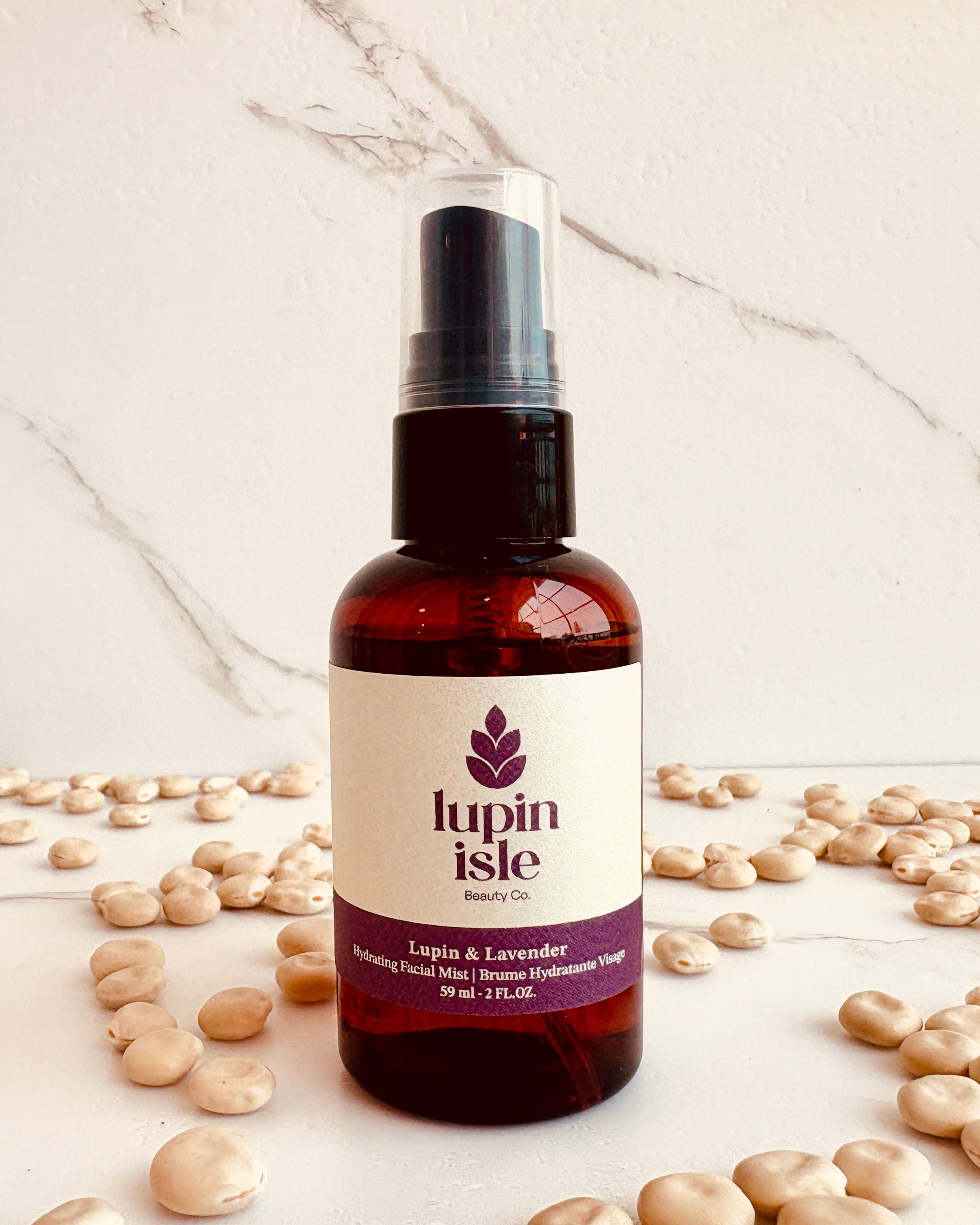 A bottle of Lupin Isle Facial Mist with a black spray top and white label, surrounded by scattered lupin beans on a white marble surface.