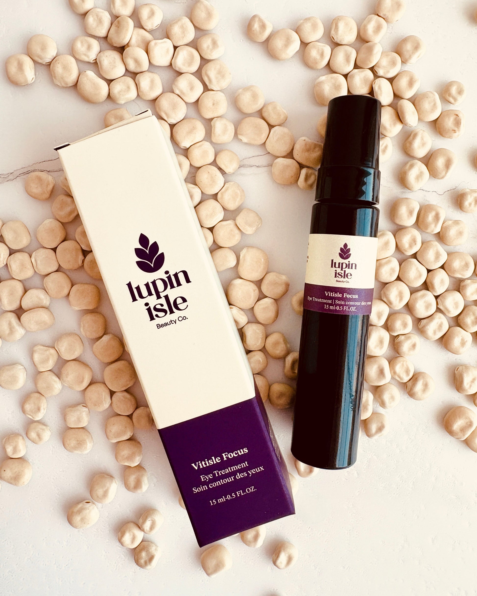 Lupin Isle Vitale Focus eye treatment shown with its white and purple box and a dark bottle, arranged on a white surface scattered with lupin beans.
