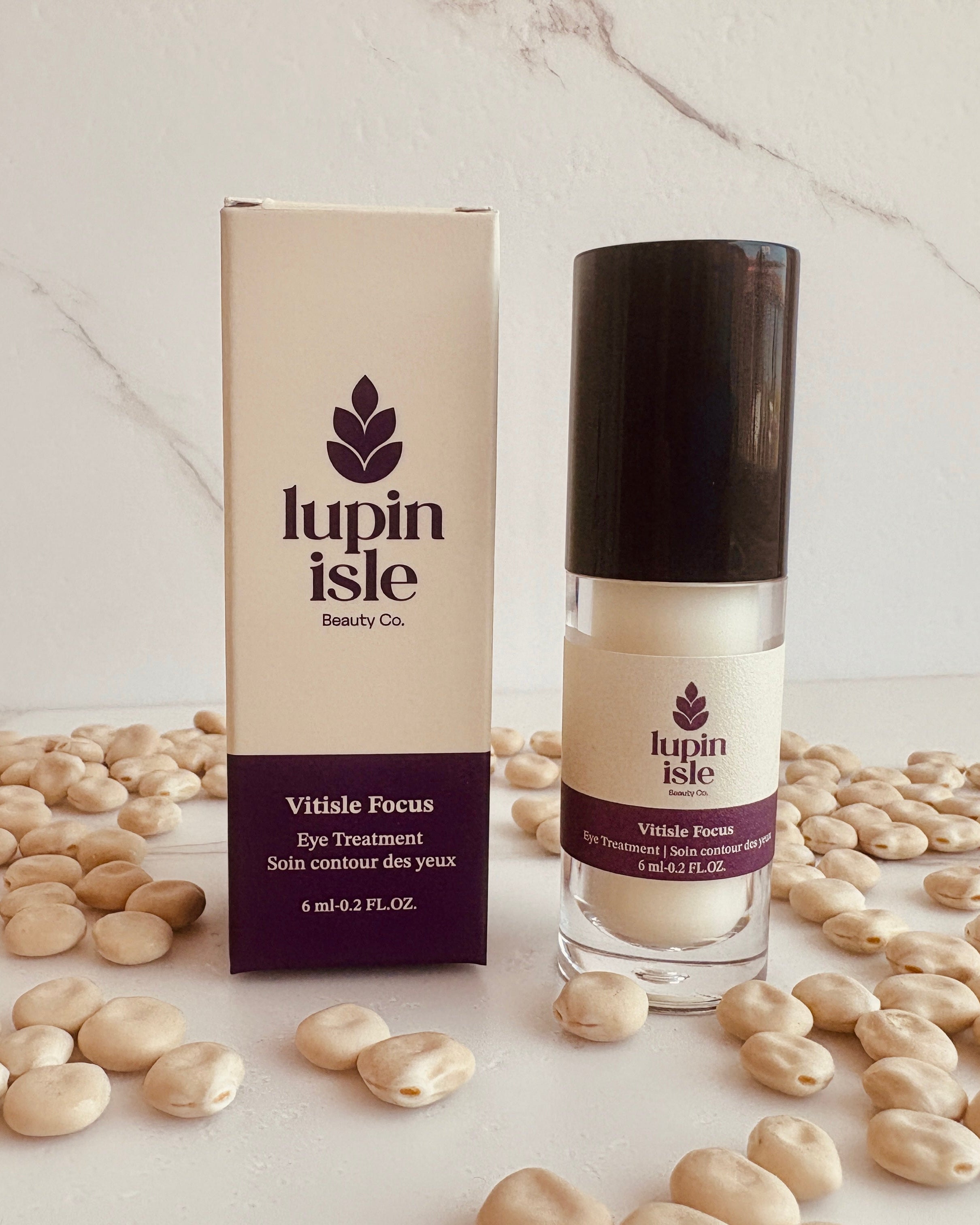 Lupin Isle Vitisle Focus eye treatment shown with its beige and purple packaging box and clear bottle with a black cap, styled on a white marble surface surrounded by scattered lupin beans.